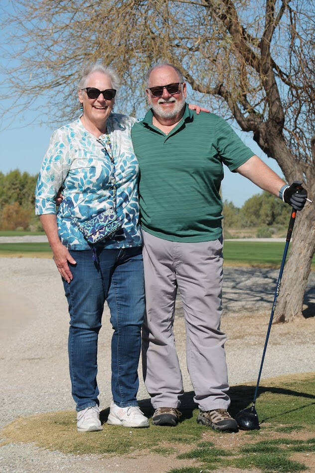 Suzy and Phil Brunell posing with a pair of golf clubs